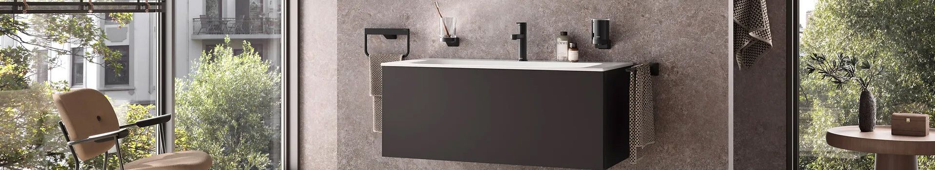 Moderner Waschtisch mit schwarzem Unterschrank vor grauer Wand in einem hellen Badezimmer mit Stuhl und Pflanzen im Hintergrund.